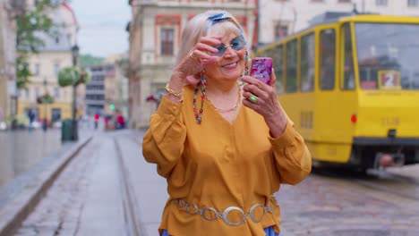 Senior-man-tourist-with-retro-photo-camera,-smiling,-listening-music-earphones,-dancing-on-street