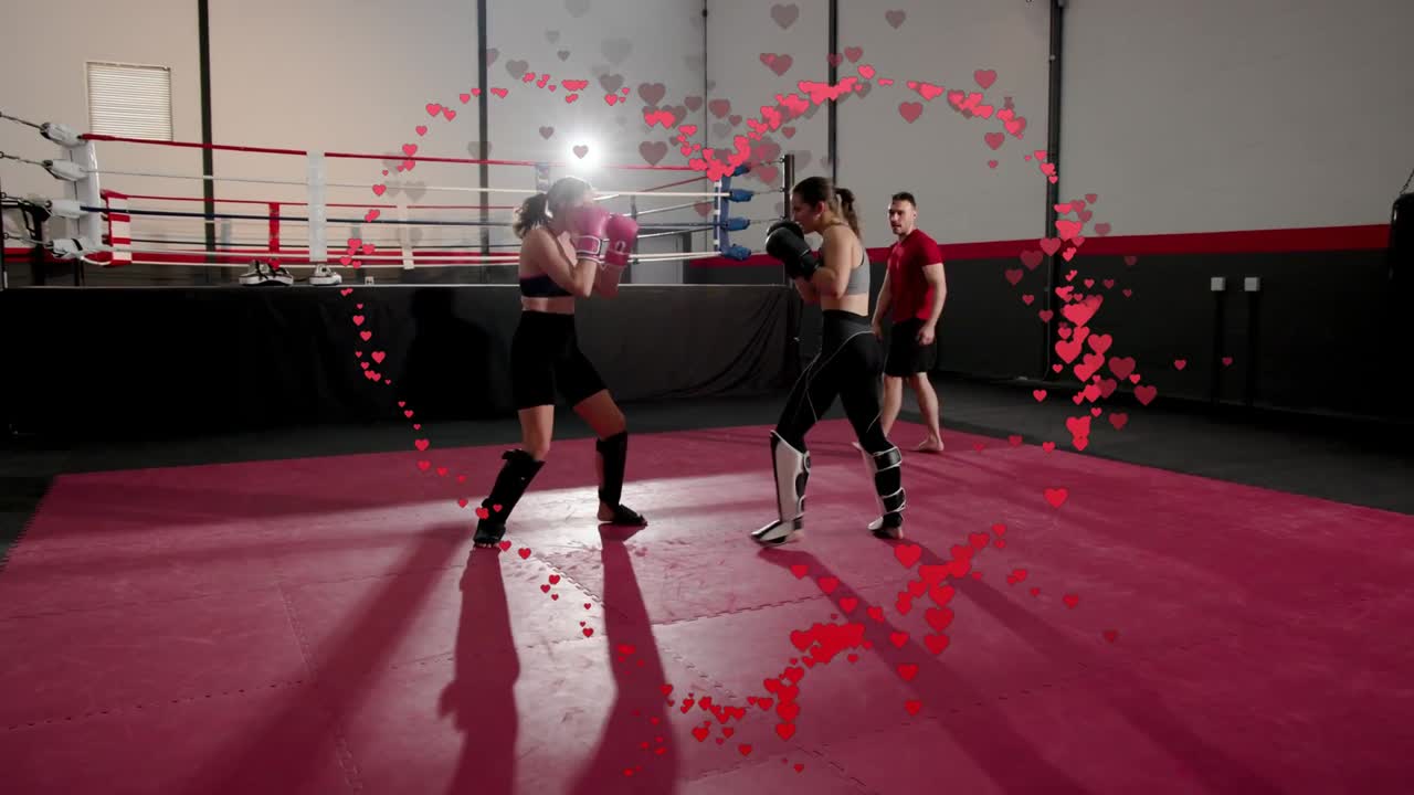 Duas boxeadoras trocando jabs e defendendo chutes no tatame, com o treinador orientando o sparring, em um treino intenso e dinâmico.