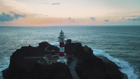 Panorámica-Aérea-Alrededor-Del-Antiguo-Faro-Blanco-Histórico-Junto-Al-Océano-Azul-Brillante,-España-Costera