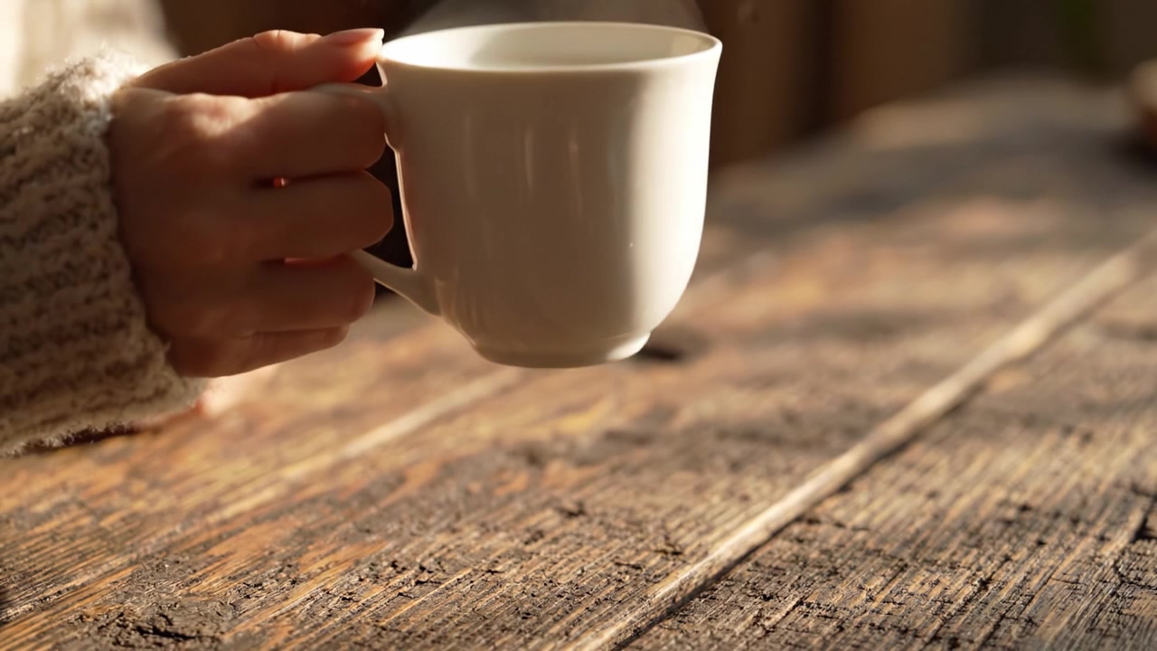 Un momento sereno catturato: vapore che sale da una tazza bianca calda su un tavolo di legno rustico, evocando comfort e relax in un'atmosfera accogliente.