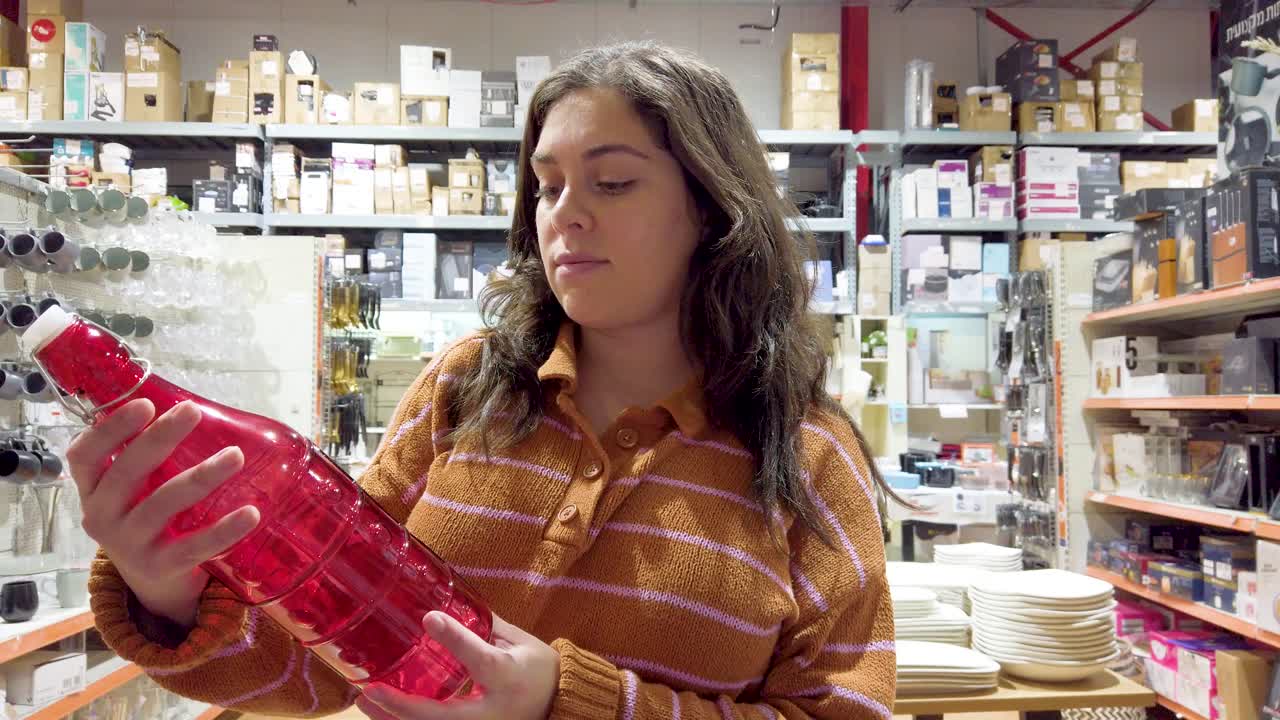 A woman is shopping in a store and is looking at a bottle of wine
