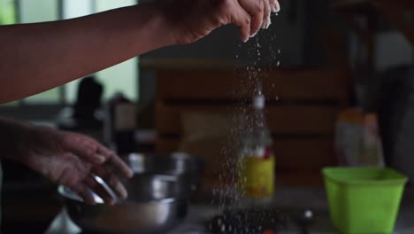 Harina-Blanca-Seca-Espolvoreada-A-Mano-Directamente-Sobre-Masa-Recién-Levantada-En-Preparación-Para-Amasar-Sobre-Una-Mesa-De-Madera,-Filmada-En-Cámara-Lenta