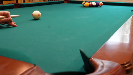 person breaks pool balls on 8 ball triangle rack and makes the 2 ball in the corner pocket closeup on the spot with solid and stripped billiard balls on table with green felt and wooden cue stick