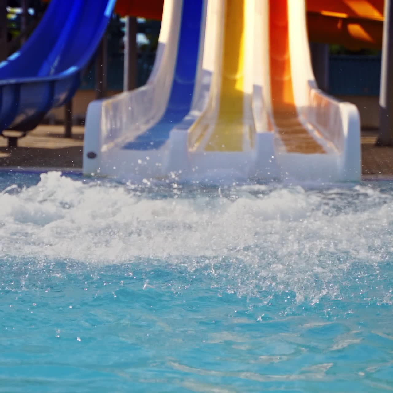 Colorful outdoor water park in summer. Cute boy riding on a slider in the water park. Water splash in the pool. Fun and happiness. Slow motion.