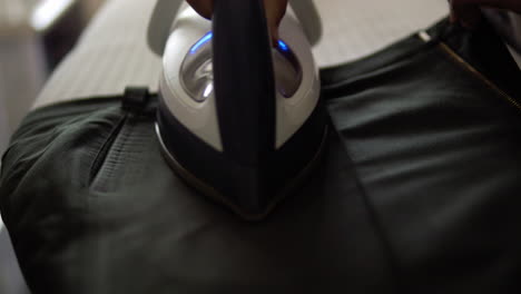 close-up of an individual ironing a pair of black trousers using a flat iron on an ironing board