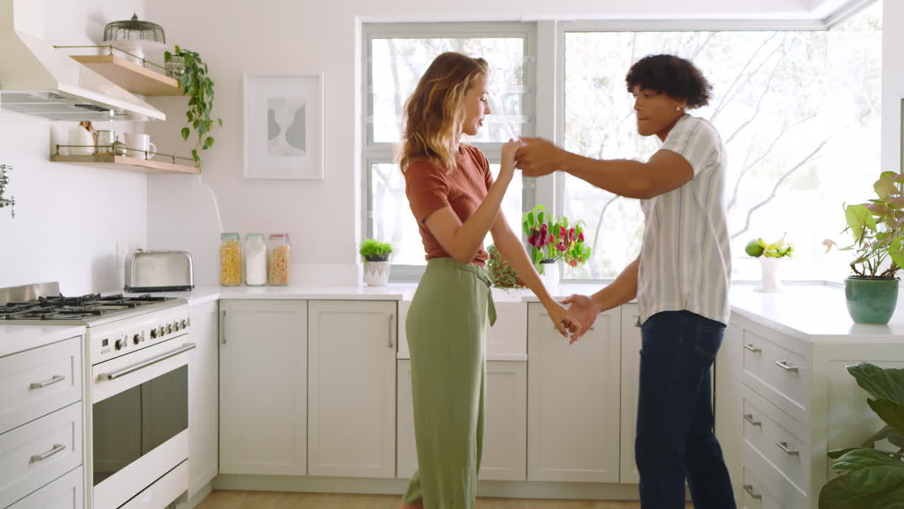 Happy diverse couple dancing together in bright kitchen, enjoying morning routine, at home