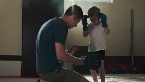 kid kicks hand pad with instructor support in martial arts gym. involved trainer teaches toddler boy fighting techniques in sports center slow motion