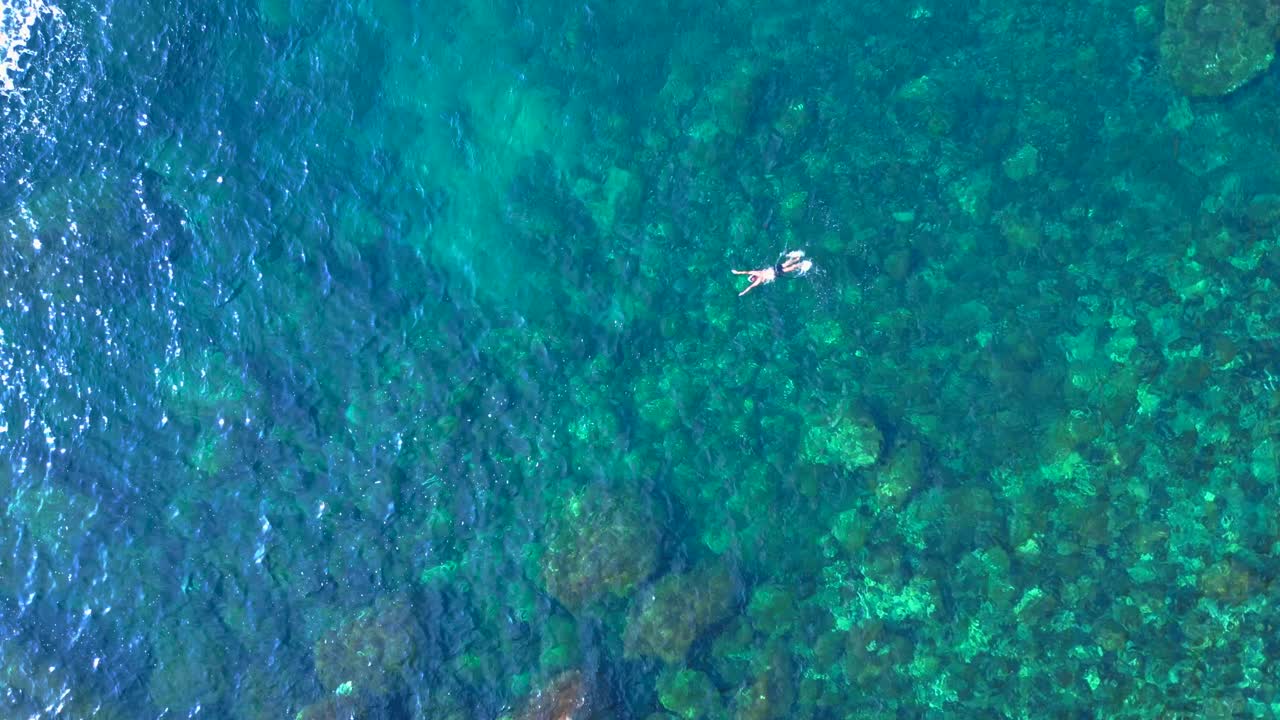 Male tourist swimming in the transparent waters of a bay in Ibiza, Spain. Fantastic aerial view flight drone camera pointing down