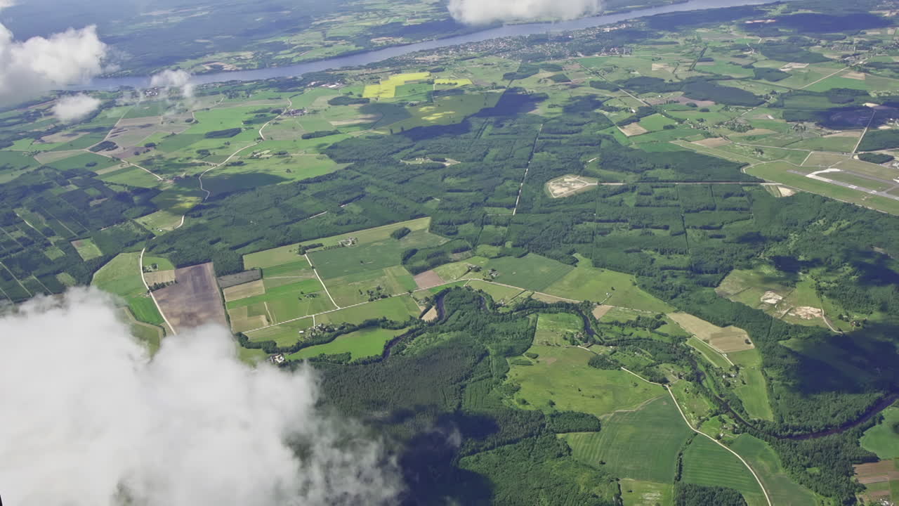 toma aérea de arriba hacia abajo de nubes flotantes en primer plano y campos verdes y bosques con río en el valle