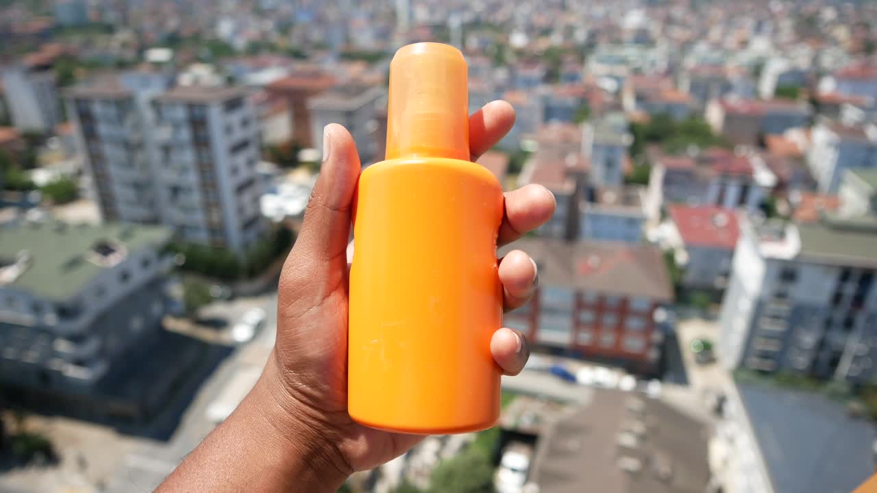 Hand holding a bottle of sunscreen with a city view in the background