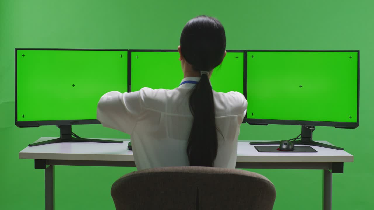 mujer sentada en un escritorio con múltiples monitores de pantalla verde