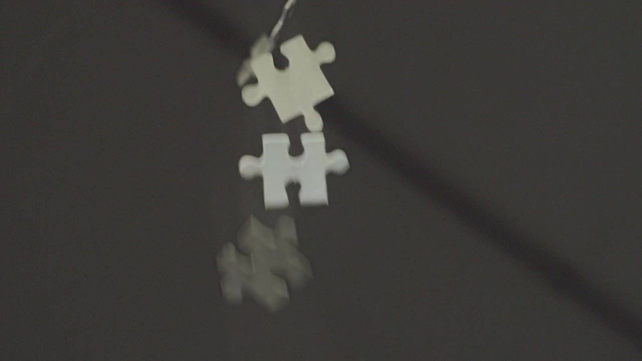 Pezzi di puzzle bianchi che cadono e ruotano al rallentatore su uno sfondo grigio. Entrano ed escono dalla messa a fuoco con profondità di campo ridotta dal soffitto