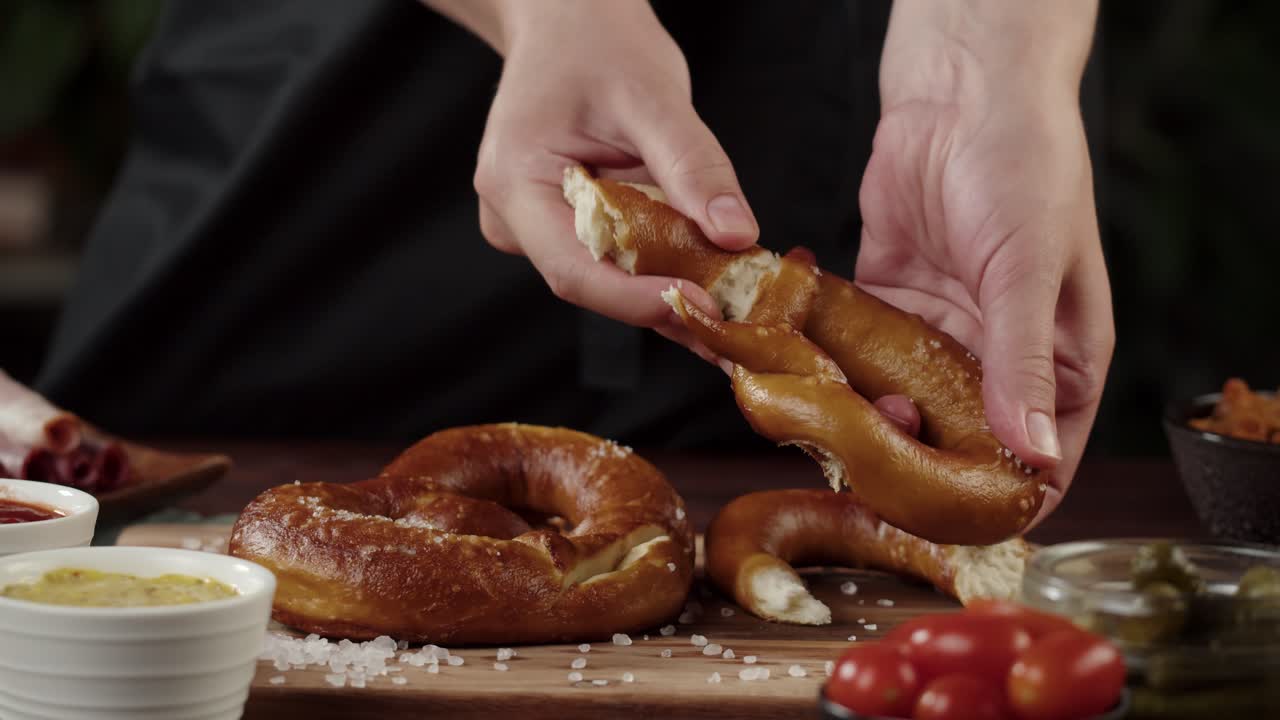 Mani che spezzano un pretzel salato appena sfornato
