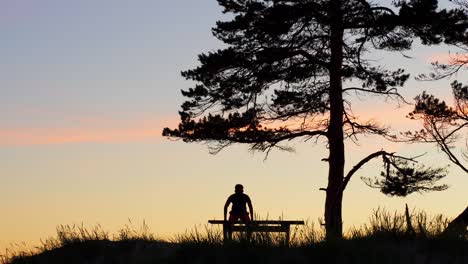 Silhouette-Eines-Einsamen,-Depressiven-Mannes,-Der-Sich-Auf-Eine-Bank-Setzt,-Farben-Des-Sonnenuntergangs