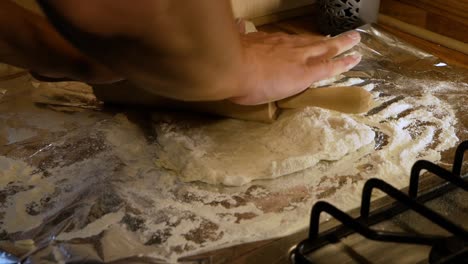 Amateur-pizza-maker-stretching-the-pizza-dough-using-wooden-rolling-pin-in-domestic-kitchen