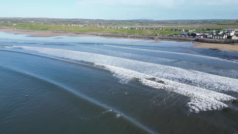 Toma-Aérea-De-Seguimiento-De-Surfistas-Montando-Una-Gran-Ola-En-La-Playa-De-Lahinch,-Irlanda