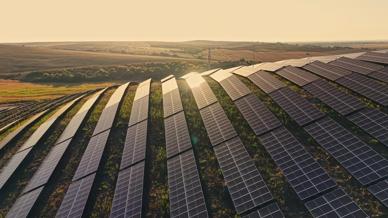 Solpaneler dækker bølgende bakker under solnedgangen i et landområde, reflekterende lys over landskabet, samtidig med at de bidrager til vedvarende energiproduktion.