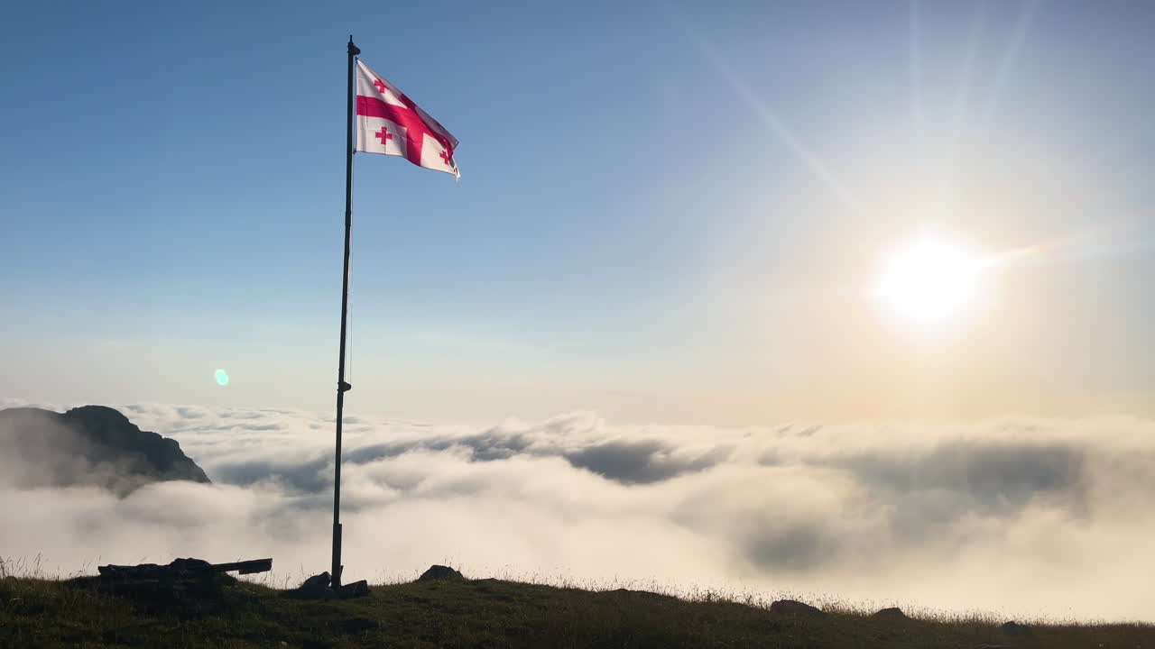 image of georgian flag waving at the summit, national flag among the clouds