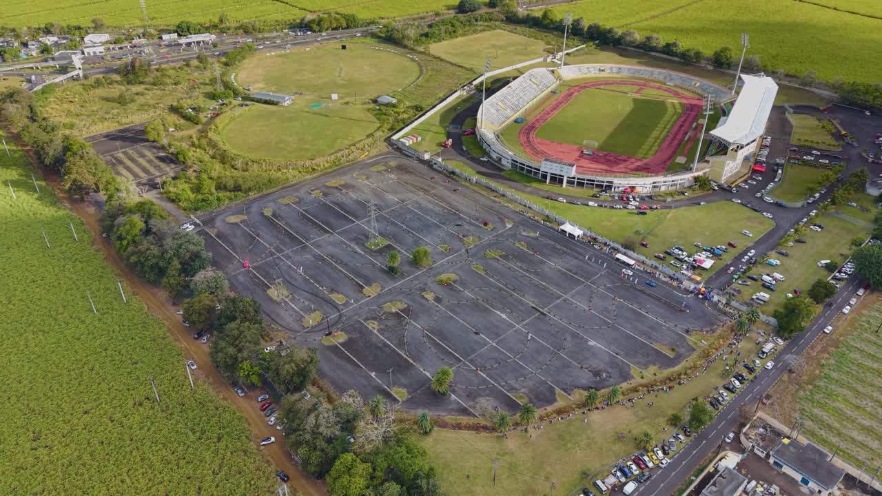 Aerial view over the Stade Anjalay in Mauritius, highlighting the huge car park covered in tire marks from a high-speed racing or drifting event next to the main stadium