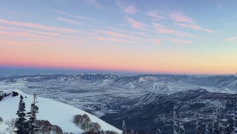 panning right shot of a stunning winter landscape scene looking down at a cloudy snow covered valley during a golden sunset from the summit of a ski resort in the rocky mountains of utah