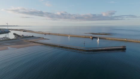 panning drone clip of sailing boats entering calm harbour haven in north sea