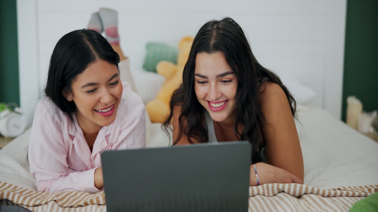 Two women using a laptop in bed