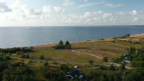 Rising-footage-of-seashore.-Houses-on-edge-of-forest-and-grassland-along-coast.-Rippled-water-surface.-Denmark