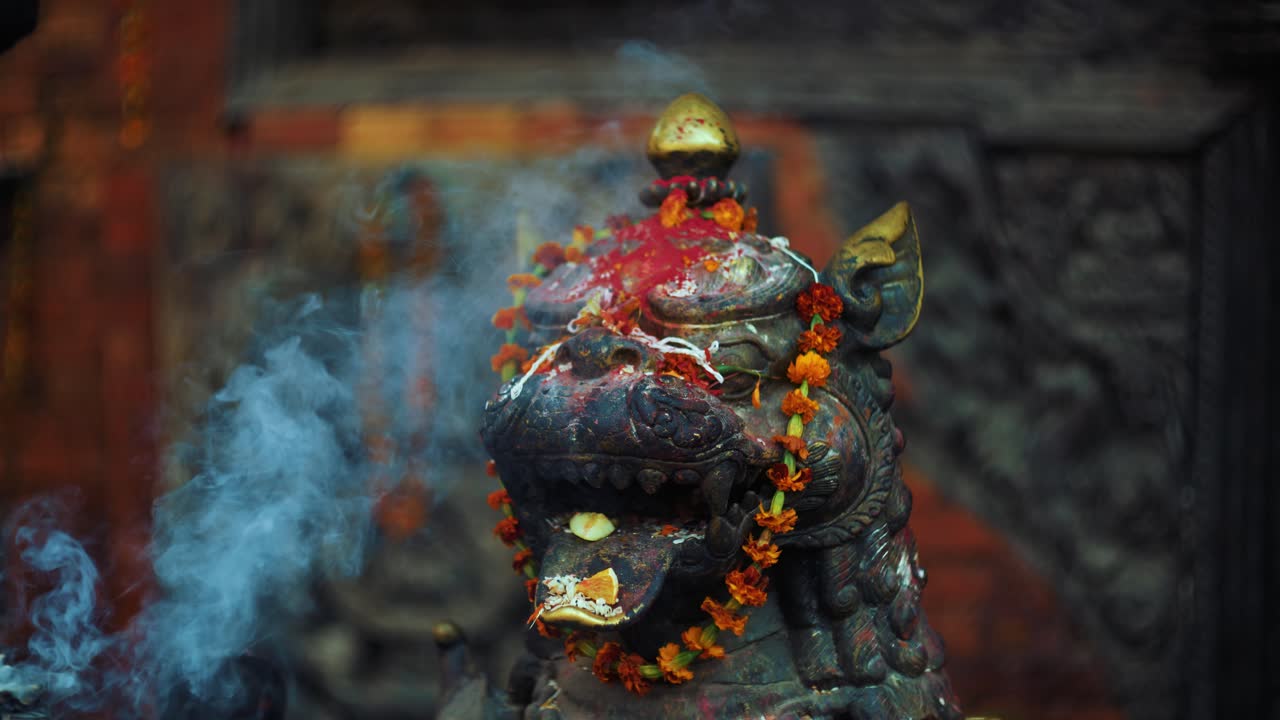 Stone lion statue covered in smoke, flowers and red powder at Taumadhi Square, Bhaktapur, Nepal