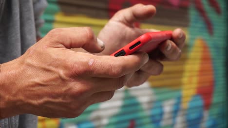 Male-hands-with-chain-bracelet-watching-video-on-cell-phone-in-street