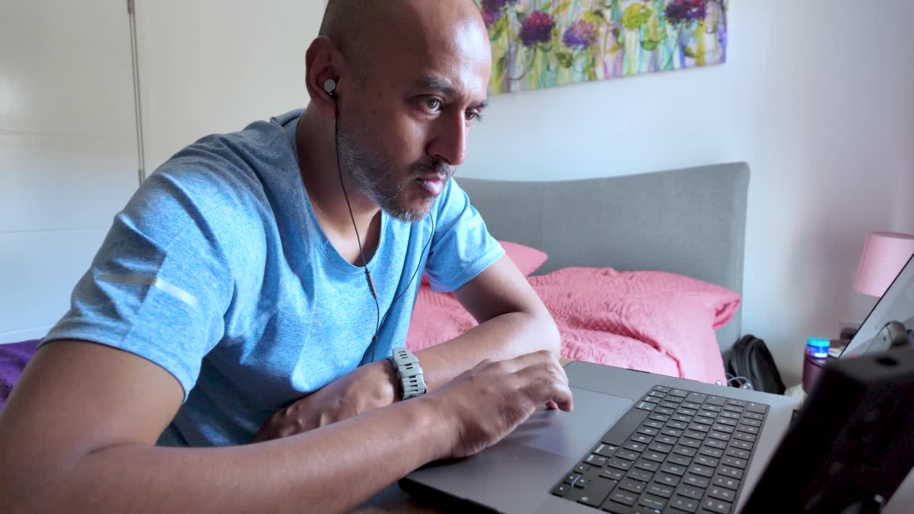 South asian man concentrating while working remotely on his laptop from the comfort of his bed