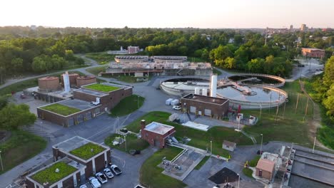 aerial shot capturing the layout of a wastewater treatment facility at dusk, with circular clarifiers and green-roofed buildings