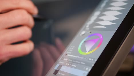 un artista o diseñador digital independiente que selecciona un tono de color y pinta con una tableta gráfica de dibujo y un bolígrafo en un estudio de arte