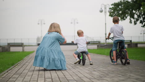 a heartwarming moment of a mother patting her little boy's back as he rides a bicycle with his older brother on a interlocked path