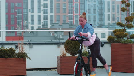 Chica-Atlética-Realizando-Ejercicios-De-Entrenamiento-Aeróbico-En-Bicicleta-Estática-En-El-Techo-De-La-Casa