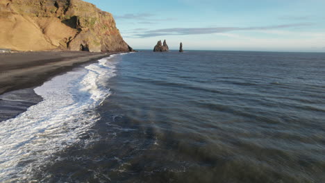 waves crashing on shore of black sand beach in iceland southern coast with jagged rock formations in background