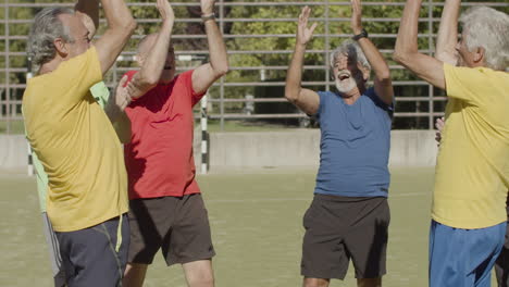 felices jugadores de fútbol senior en círculo juntando las manos y aplaudiendo para celebrar la victoria