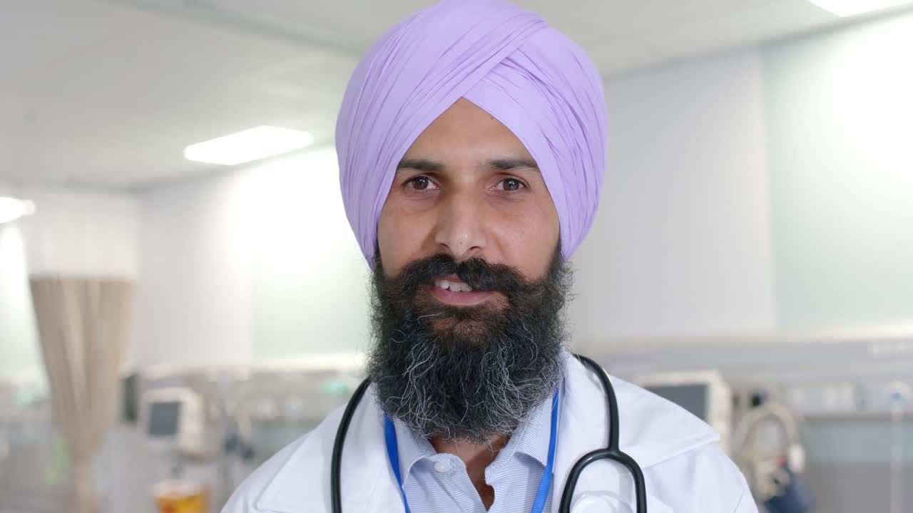 Ritratto di un medico sikh felice di etnia mista con turbante che guarda la telecamera in ospedale, al rallentatore
