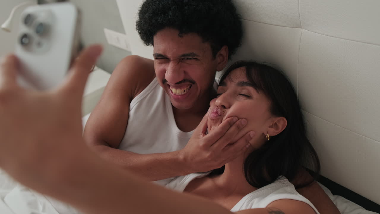 Playful Young Couple Taking a Selfie in Bed