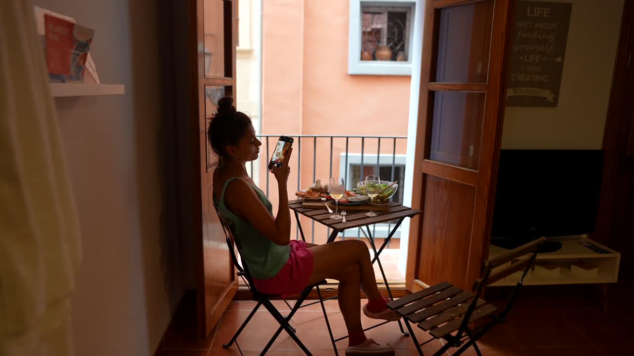 mujer disfrutando de una comida al aire libre y usando el teléfono móvil en un balcón