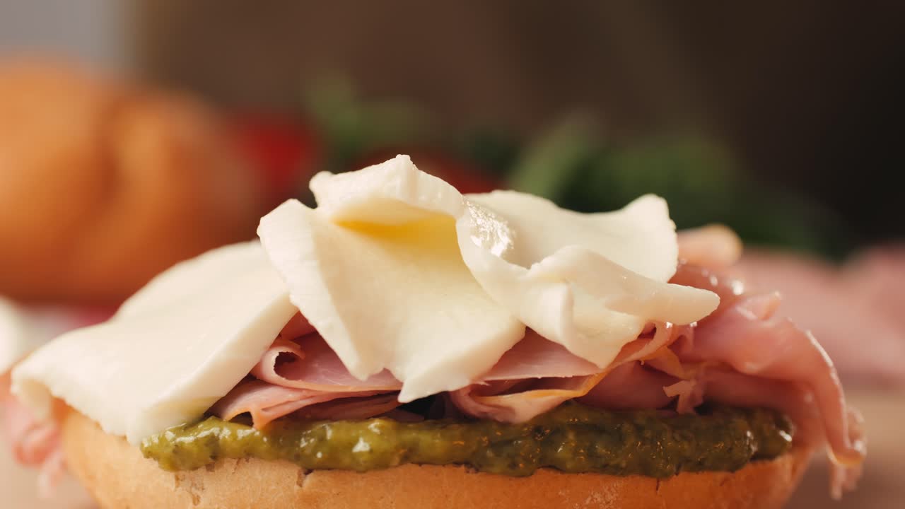 Mortadella ham sandwich, Traditional italian focaccia filled with thin pesto slices of mortadella, served by chef man in cafe restaurant. Macro of traditional italian spanish tapas antipasti.