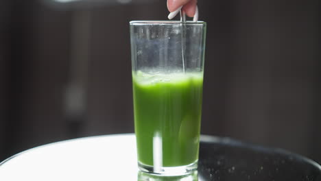 an intricately designed spoon is immersed in a smooth, vibrant green juice within a tall, slender glass, accentuated glow of diffused natural light creating subtle reflections on a glossy surface