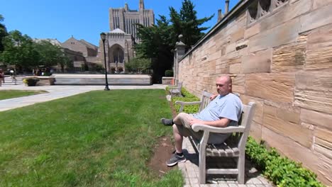 Man-walking-to-Bench-on-Campus-and-Sitting-4K