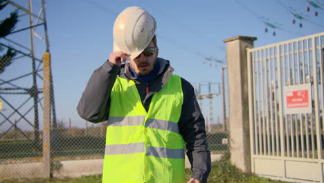 ingegnere maschio che chiude la giacca con la cerniera e indossa un casco di sicurezza hard hat alla sottostazione elettrica dinamica portatile