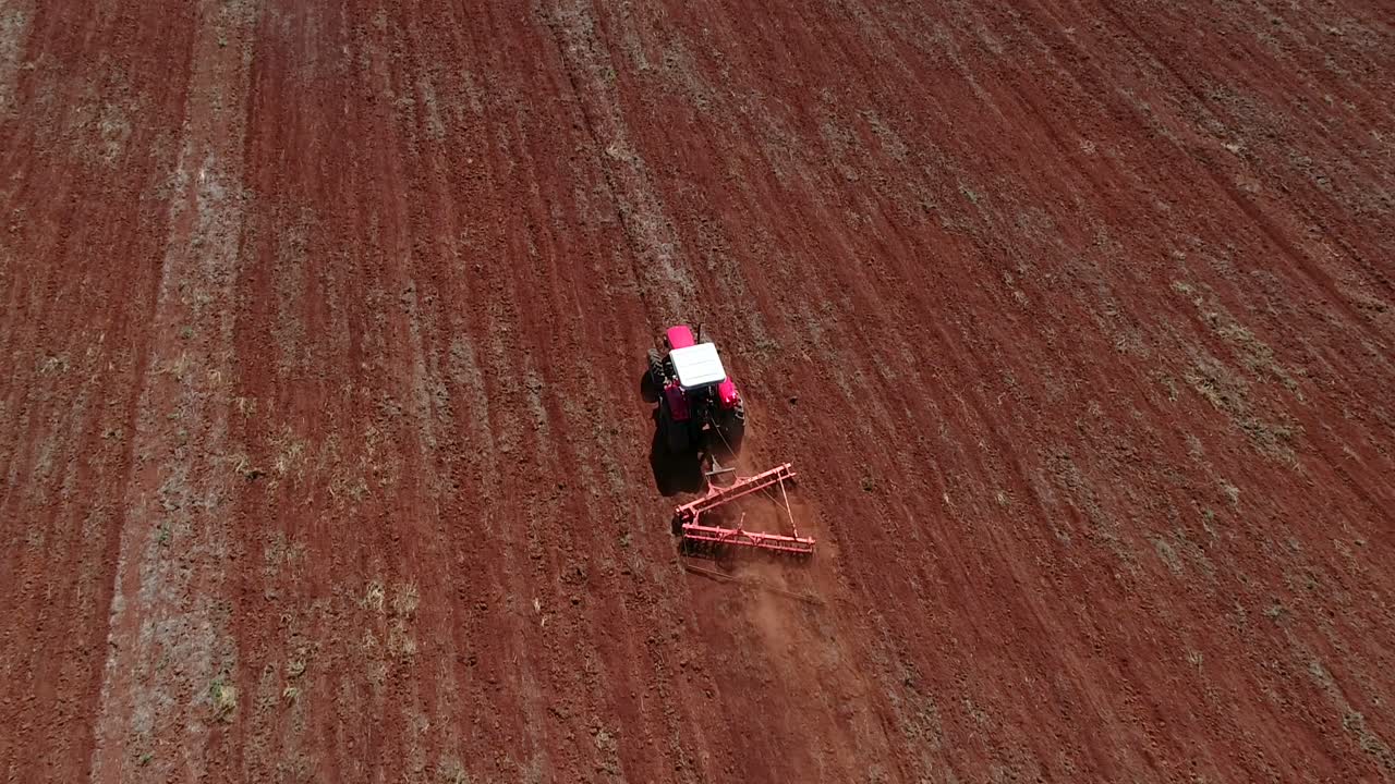 dron aéreo siguiendo por detrás de un tractor preparando el suelo para la siembra de semillas y mostrando todo el campo