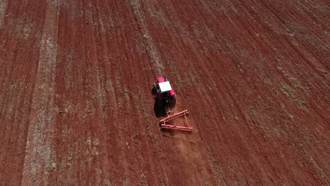 aerial drone following from behind a tractor preparing the soil for seed planting and showing whole field