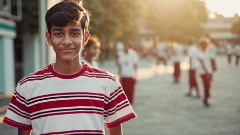 student smiling confidently at camera while classmates playing in background, golden sunlight illuminating schoolyard during afternoon break