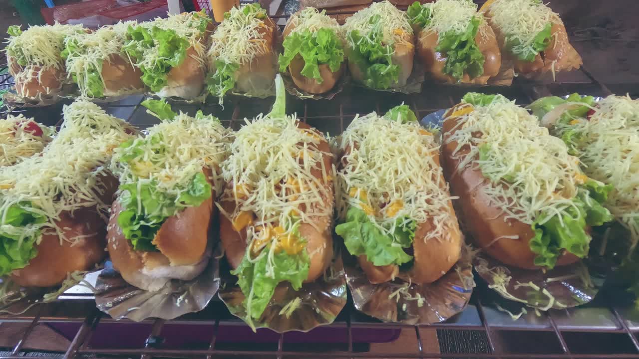 Rows of hot dog buns topped with shredded cheese and kept warm on a steaming grill at a street food stall