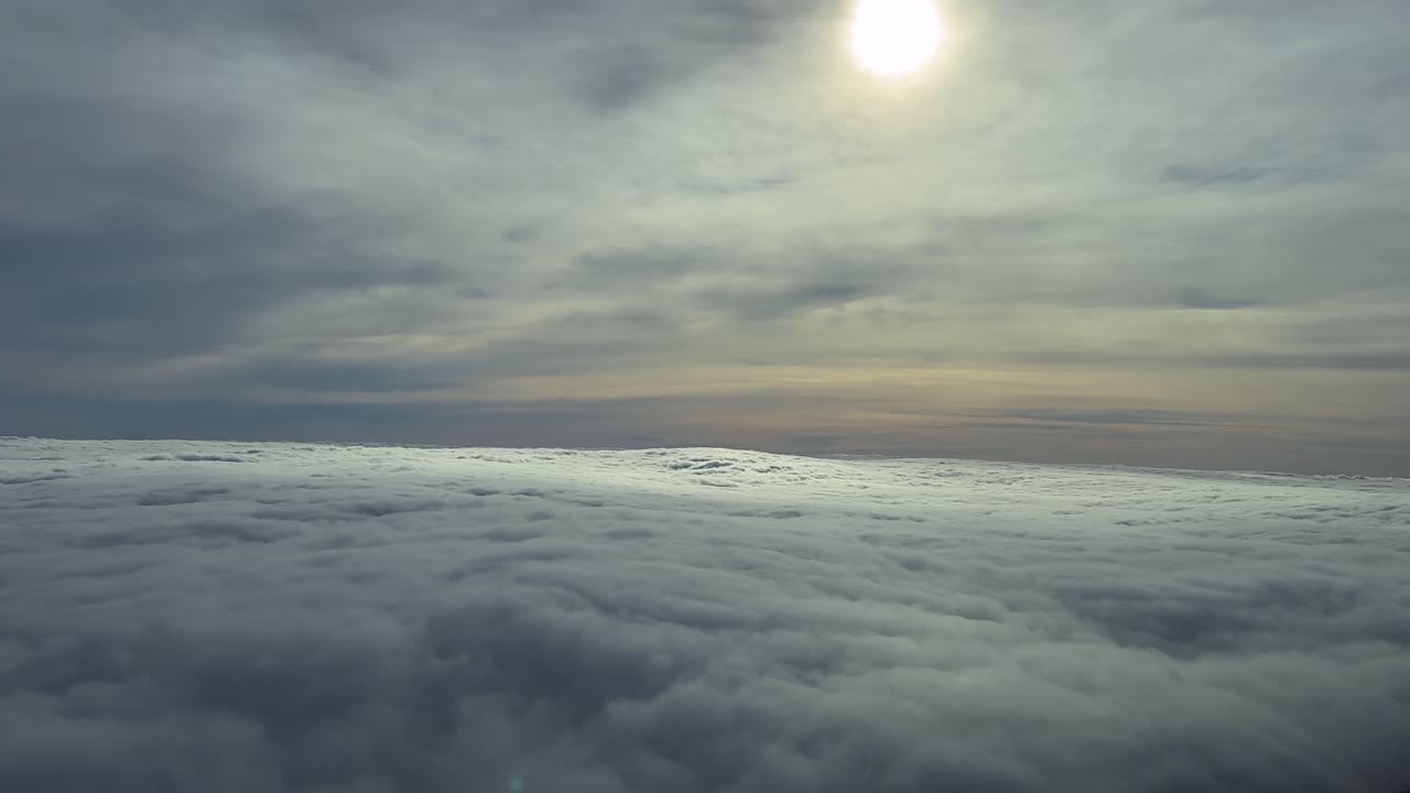 Uma vista imersiva da perspetiva de um piloto enquanto voa entre camadas infinitas de nuvens estratos etéreas com um sol esmaecido velado por nuvens mais altas