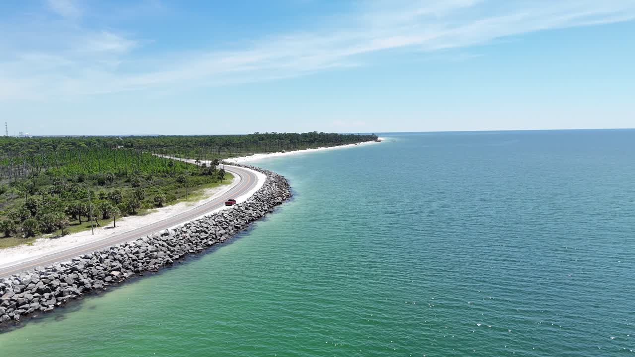 Drone orbit at stone breakwater on coastline road curving along with natural environment, Cape San Blas, Gulf County, Florida, USA