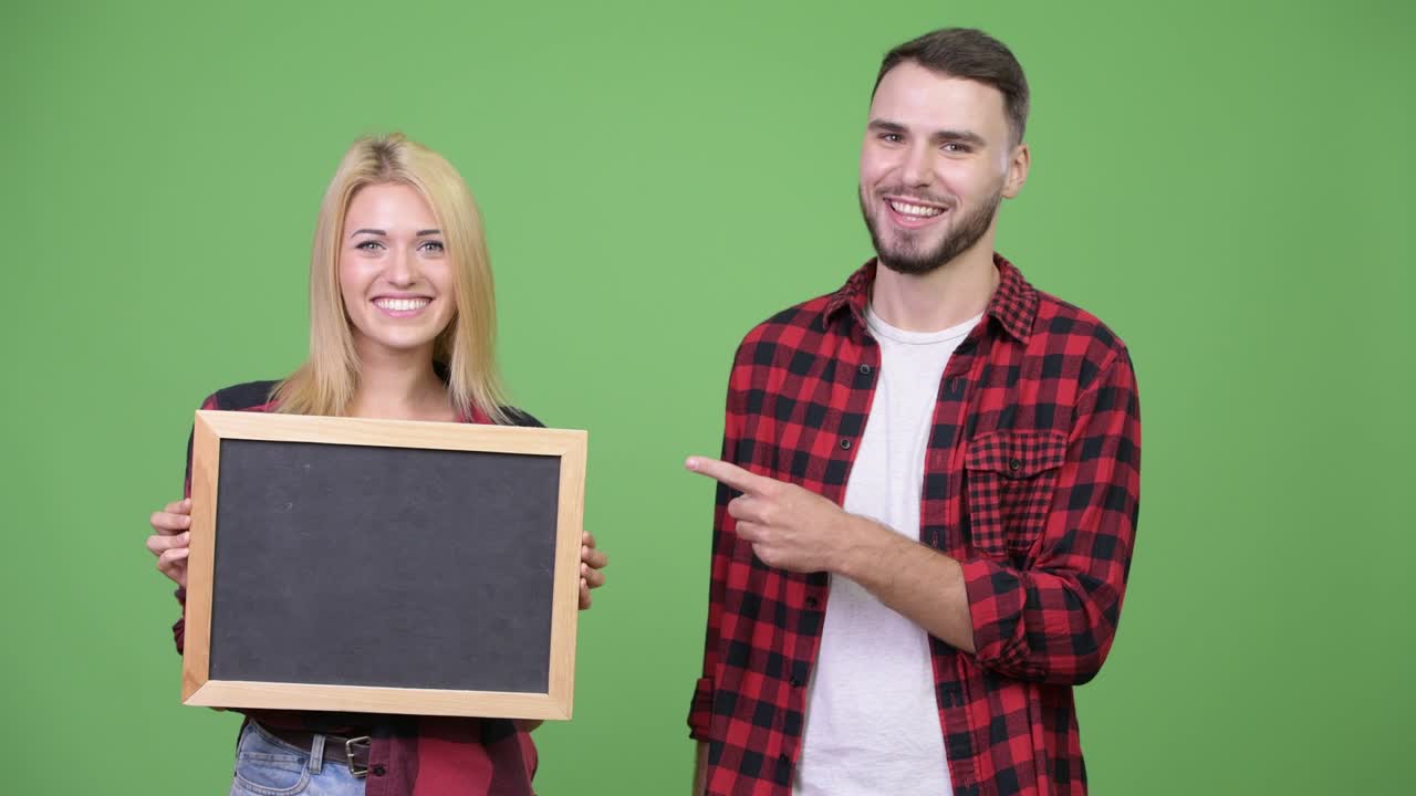Young couple holding blackboard and pointing finger together
